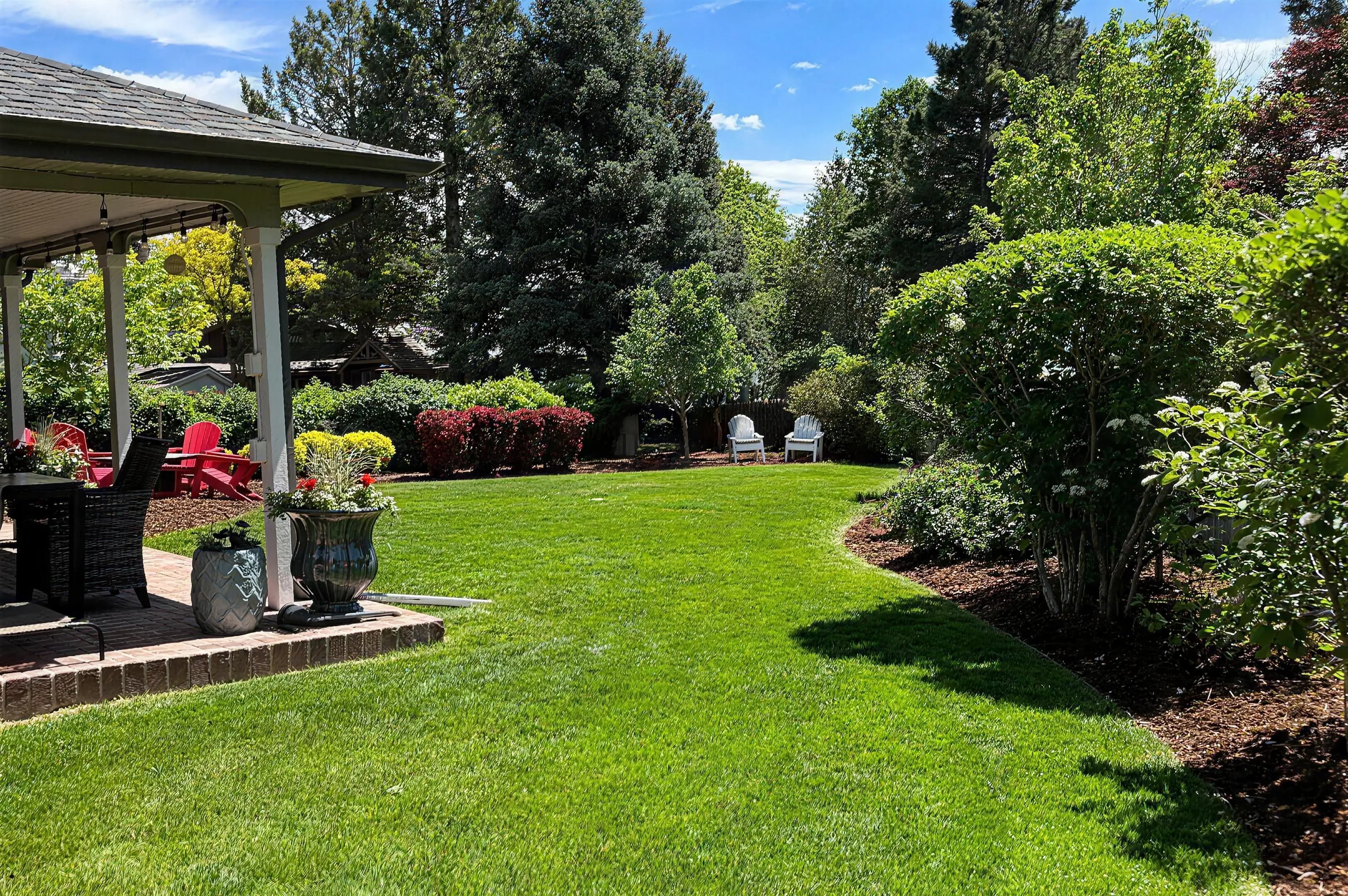 Manicured backyard lawn bordered by mulched shrub beds, with a covered patio and planted containers